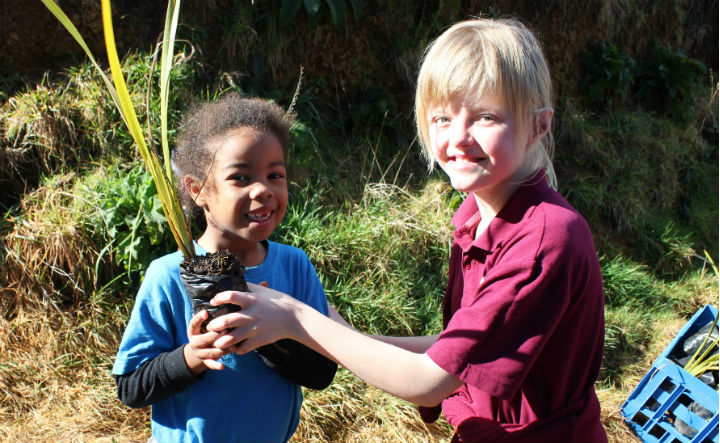 Two children holding trees to be planted.